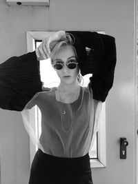 Portrait of young woman wearing sunglasses while standing against door