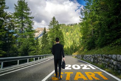 Rear view of man standing on road against trees