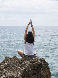 Rear view of woman meditation on rock against sea