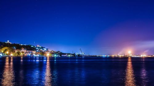 Illuminated city by sea against blue sky at night