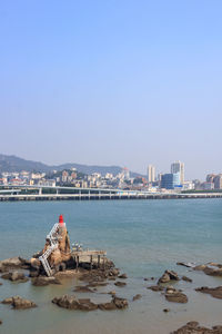 Sea by cityscape against clear sky