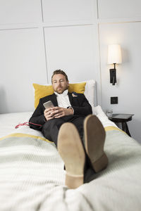 Businessman relaxing on bed while listening to music from mobile phone in hotel room