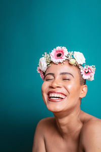 Close-up of young woman wearing flowers against blue background