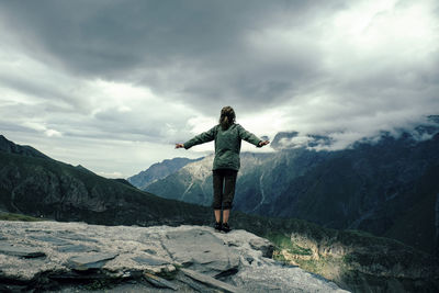 Rear view of woman with arms outstretched standing on mountain against cloudy sky