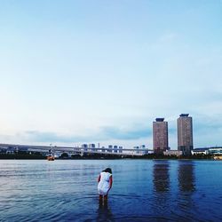 Rear view of woman standing in river at city against sky