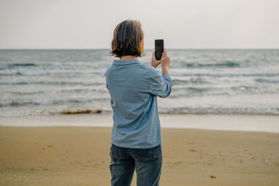 A young woman on the beach near the ocean in the spring at sunset takes a selfie, talks via video