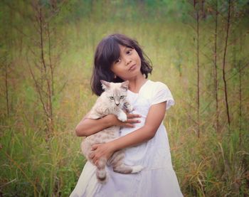 Portrait of cute girl holding cat against while standing on field