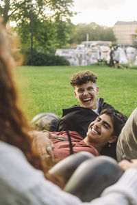 Happy male friends laughing together while talking with friend at park