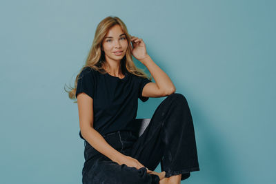 Portrait of young woman standing against blue background