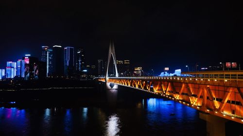 Illuminated bridge over river by buildings against sky at night