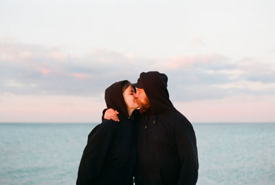 Young woman standing against sea against sky during sunset