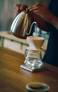 Midsection of person pouring coffee in cup on table