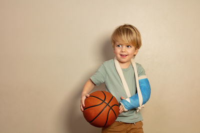 Portrait of girl playing basketball while standing against wall