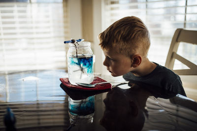 Boy looking in jar on table while sitting at home