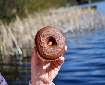 Close-up of hand holding donut against water