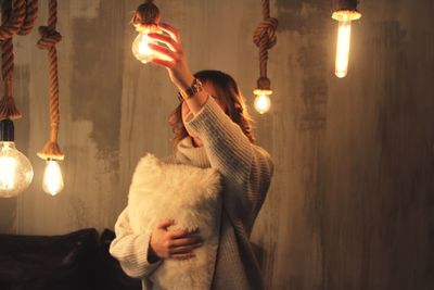 Young woman holding illuminated light bulb at night