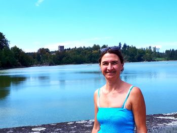 Portrait of smiling mature woman standing against lake