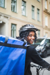 Portrait of smiling delivery woman with bag in city
