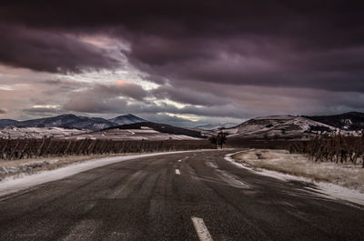 Scenic view of road by mountains against dramatic sky