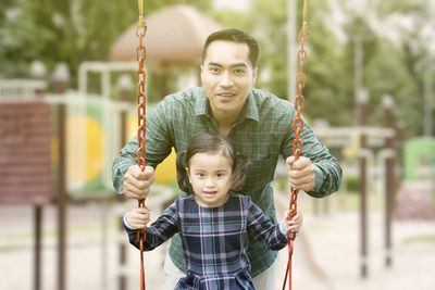 Portrait of father and daughter by swing in playground