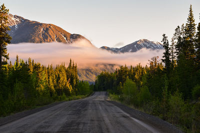 Empty road along trees and mountains against sky