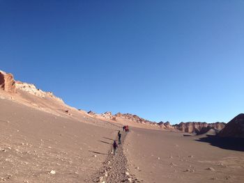 People walking on barren landscape against blue sky