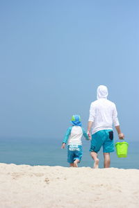 Rear view of friends walking on beach against clear blue sky