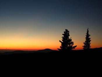 Silhouette trees on landscape against clear sky at sunset