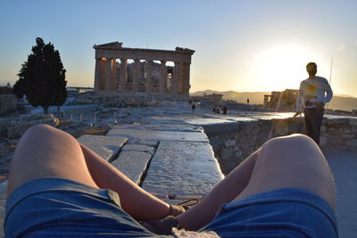 Low section of man with friend visiting parthenon against clear sky during sunset