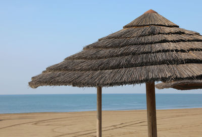 Thatched roof parasol on beach against clear sky