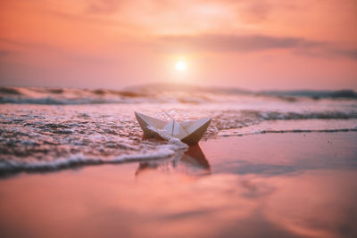 Paper boat at beach against sky during sunset