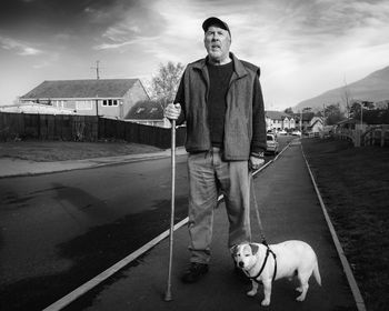 Man standing with dog on sidewalk against sky