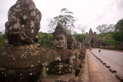 Ancient buddhist statues by road against sky