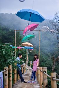 Man and woman standing by railing with umbrella hanging against mountain