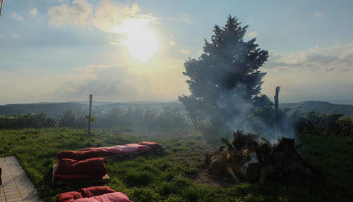 Firewood and smoke with cushions in back yard against sky