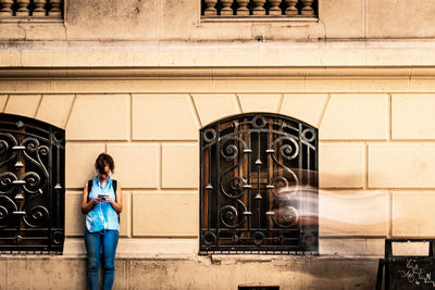 Woman using mobile phone white standing by built structure