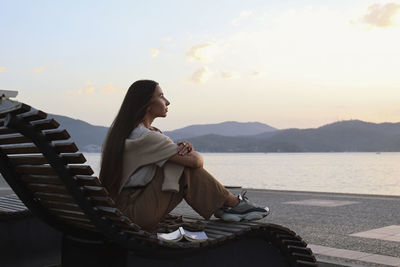 Thoughtful woman sitting on deck chair at sunset