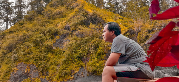 Side view of young man sitting on plant during autumn