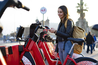 Young woman taking a rental bike with her cell phone.