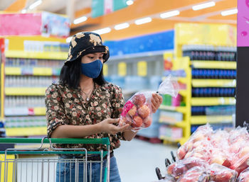 Asian woman wearing face mask shopping and choosing, looking for fruits or grocery things to buy 