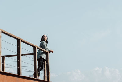 Low angle view of bird perching on roof against sky