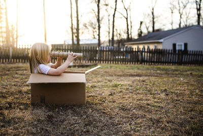 Side view of girl sitting in cardboard box on field