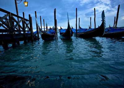 Low angle view of gondolas moored at grand canal against cloudy sky