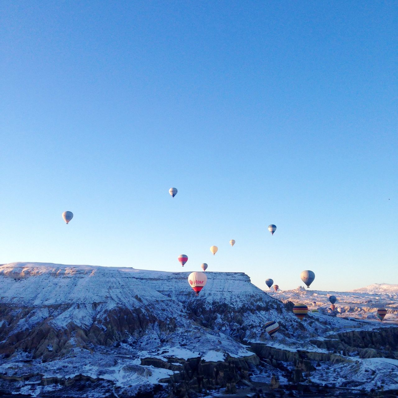 mid-air, flying, clear sky, copy space, blue, hot air balloon, scenics, mountain, low angle view, tranquility, nature, beauty in nature, parachute, paragliding, tranquil scene, rock - object, adventure, multi colored, bird, outdoors