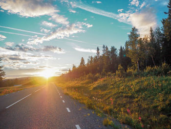 Road amidst trees against sky during sunset