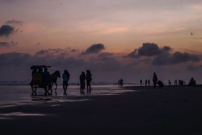 Silhouette people at beach against sky during sunset