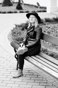 Full length portrait of young woman sitting on footpath