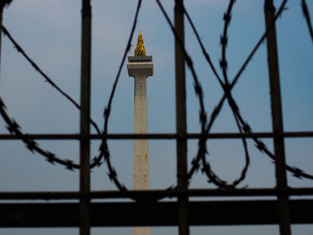 Low angle view of tower against sky seen through fence