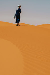 Man walking on sand dune in desert against sky