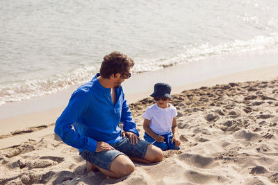 Dad and son play in sunglasses on the beach in summer in blue clothes while on vacation